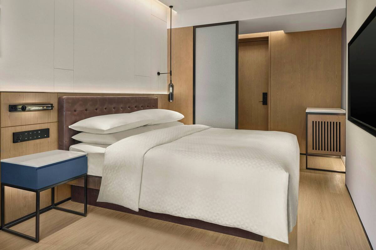 Ein modernes Hotelzimmer mit Bett, Nachttisch und Fernseher.