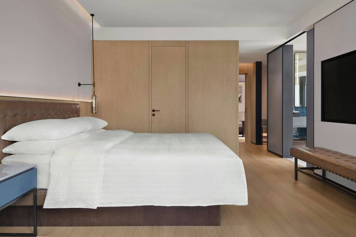 Ein modernes Hotelzimmer mit einem großen Bett, einem Nachttisch, einer Bank, einem Kleiderschrank und einem Fernseher.
