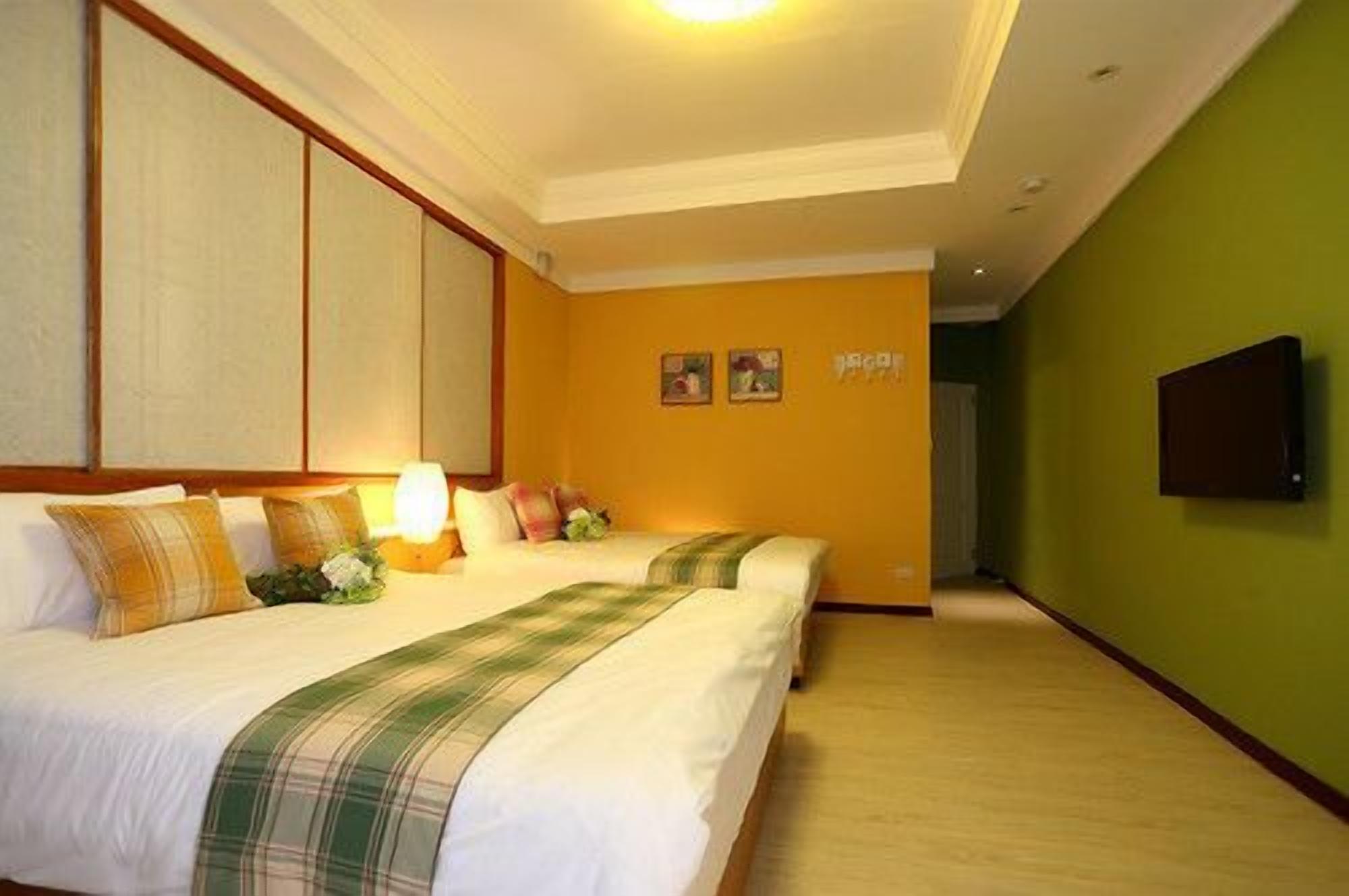 Ein Hotelzimmer mit zwei Betten, einem an der Wand befestigten Fernseher und einem Korridor mit grüner Wand.