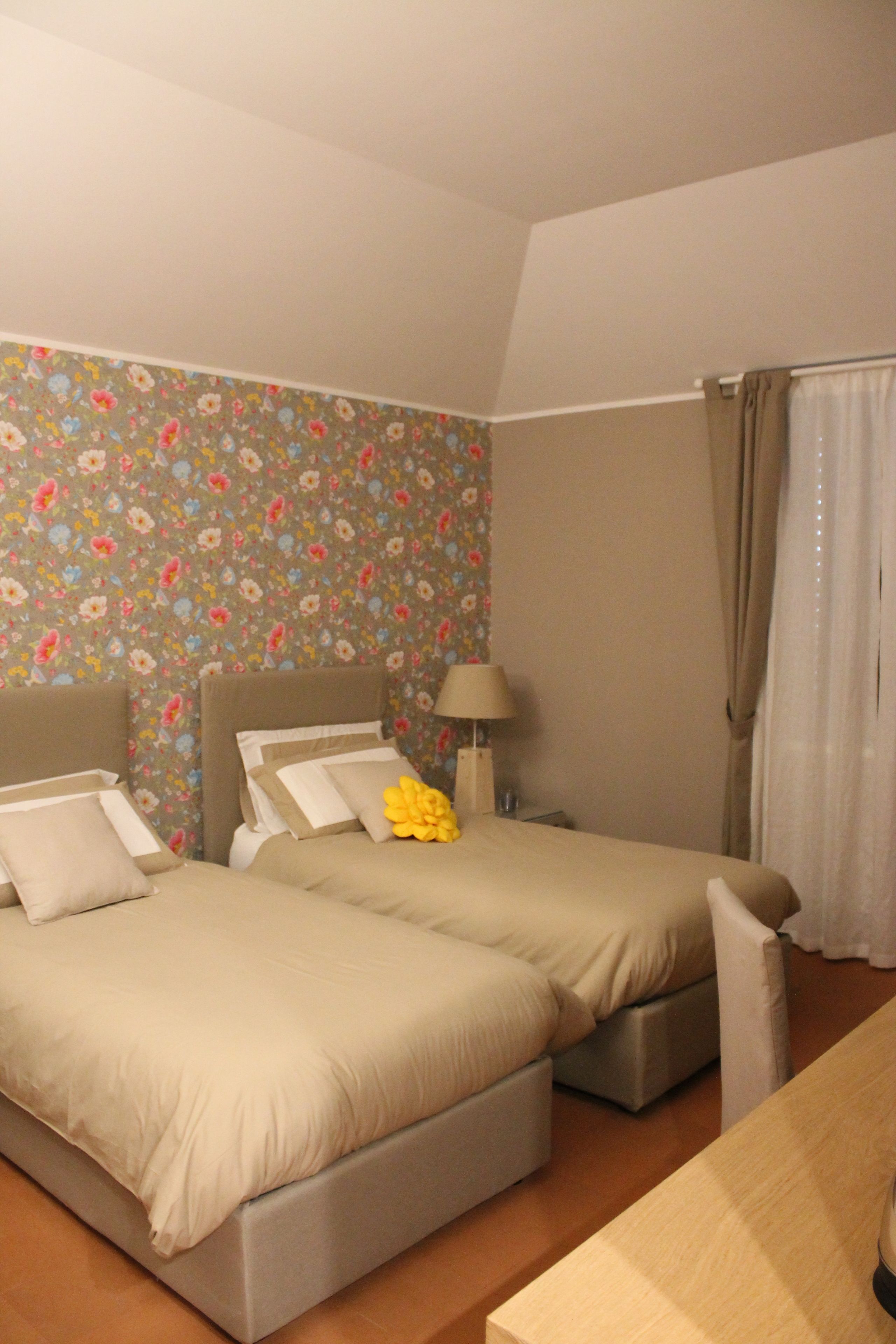 A hotel room with two beds, a nightstand, a lamp, and a window with curtains.