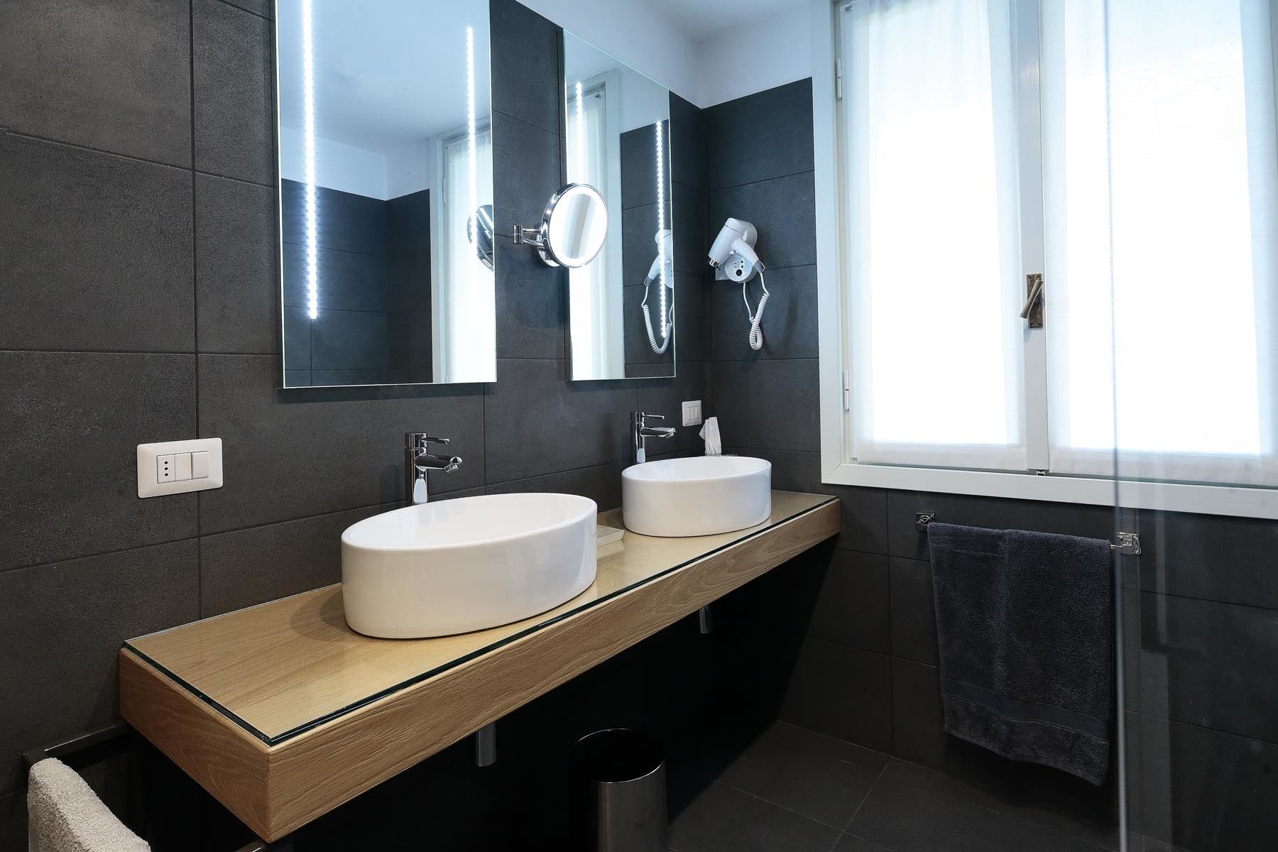 A modern bathroom with two sinks, a mirror, and a hairdryer on the wall.