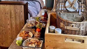 Een gezellige kamer met een bed, een eettafel met ontbijtproducten, een rieten mand met bestek en uitzicht op groen buiten.