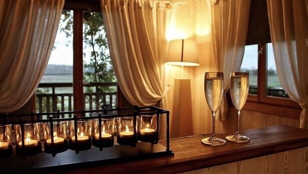 Een bar met kaarsen en twee champagneglazen, houten lambrisering en uitzicht door het raam.