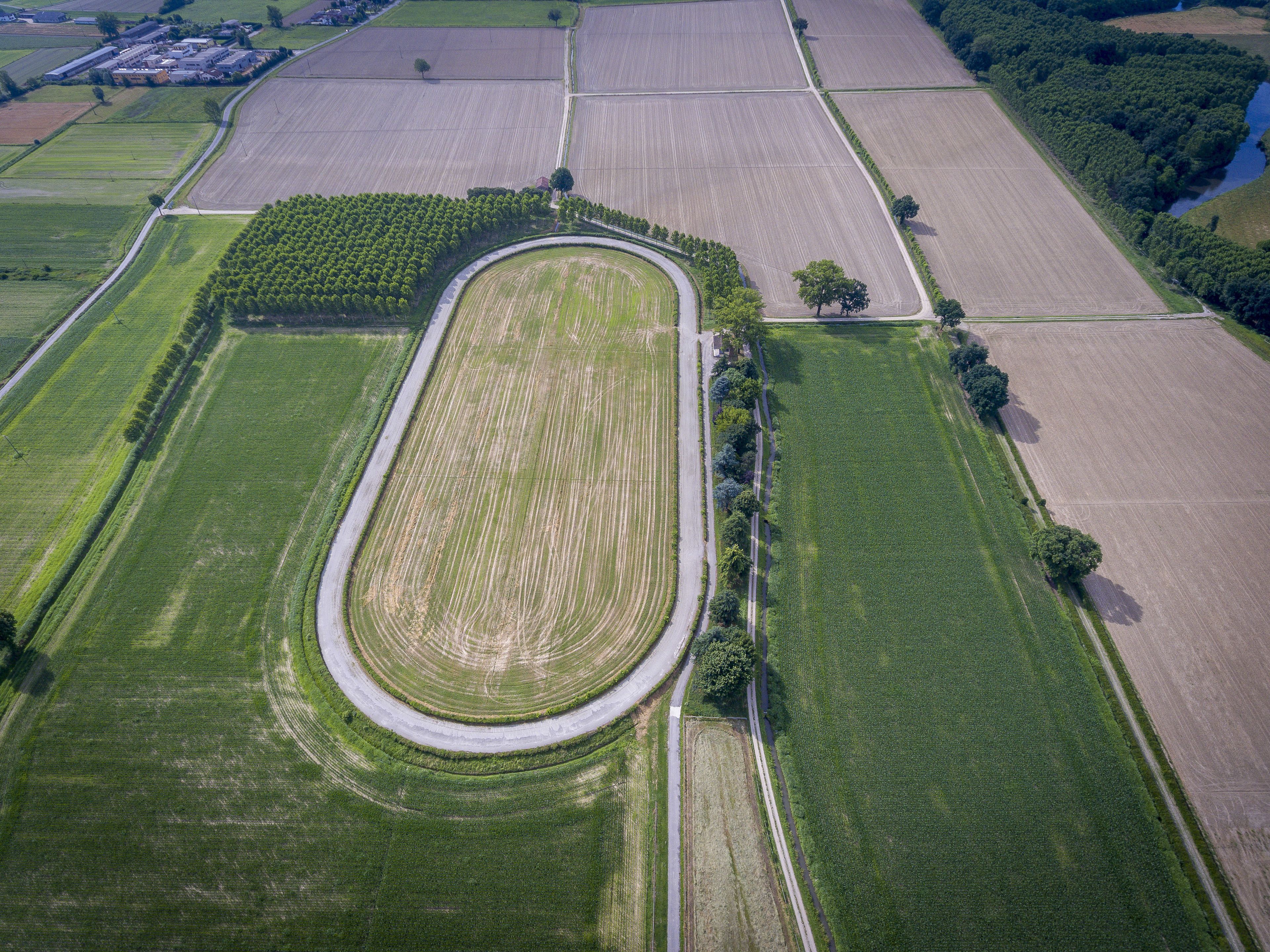 Vista aérea de un extenso campo ovalado, con una carretera serpenteando a través de él, rodeado de campos más pequeños y una zona boscosa.