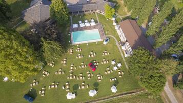 An aerial view of a property with a swimming pool, sun loungers, and a parking area.