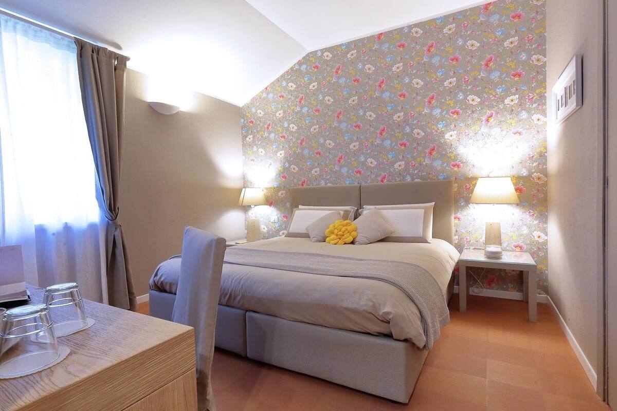 Een slaapkamer met een bed, nachtkastjes, een bureau met glazen en een raam met gordijnen.