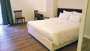 A neatly made bed in a hotel room with a wooden floor, a chair, and a nightstand with a lamp.