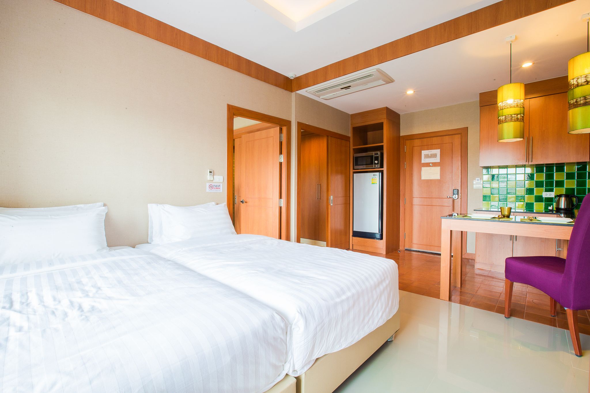 A hotel room with a bed, a desk, a chair, and a kitchenette.