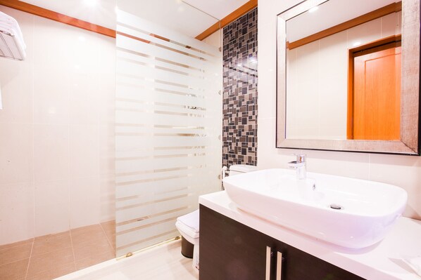 A modern bathroom with a white sink, a tiled shower area, and a wooden door.