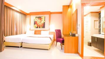 A hotel room with two beds, a desk, a chair, a painting, and a bathroom with a mirror and sink.