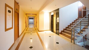 Un couloir d’hôtel avec un escalier à garde-corps en verre, des portes en bois et un sol carrelé.