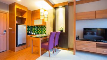 A compact kitchen with a refrigerator, a dining table with chairs, a television, and wooden cabinets.