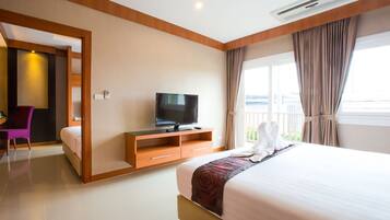 A hotel room with a bed, a TV on a wooden stand, a desk with a chair, and a balcony with curtains.