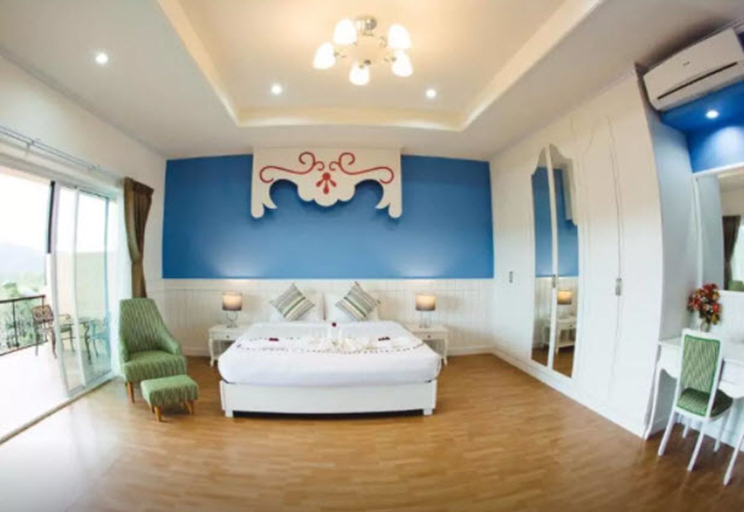 Un dormitorio con una cama grande, una silla verde, una mesita de noche con lámpara y una ventana con vistas.
