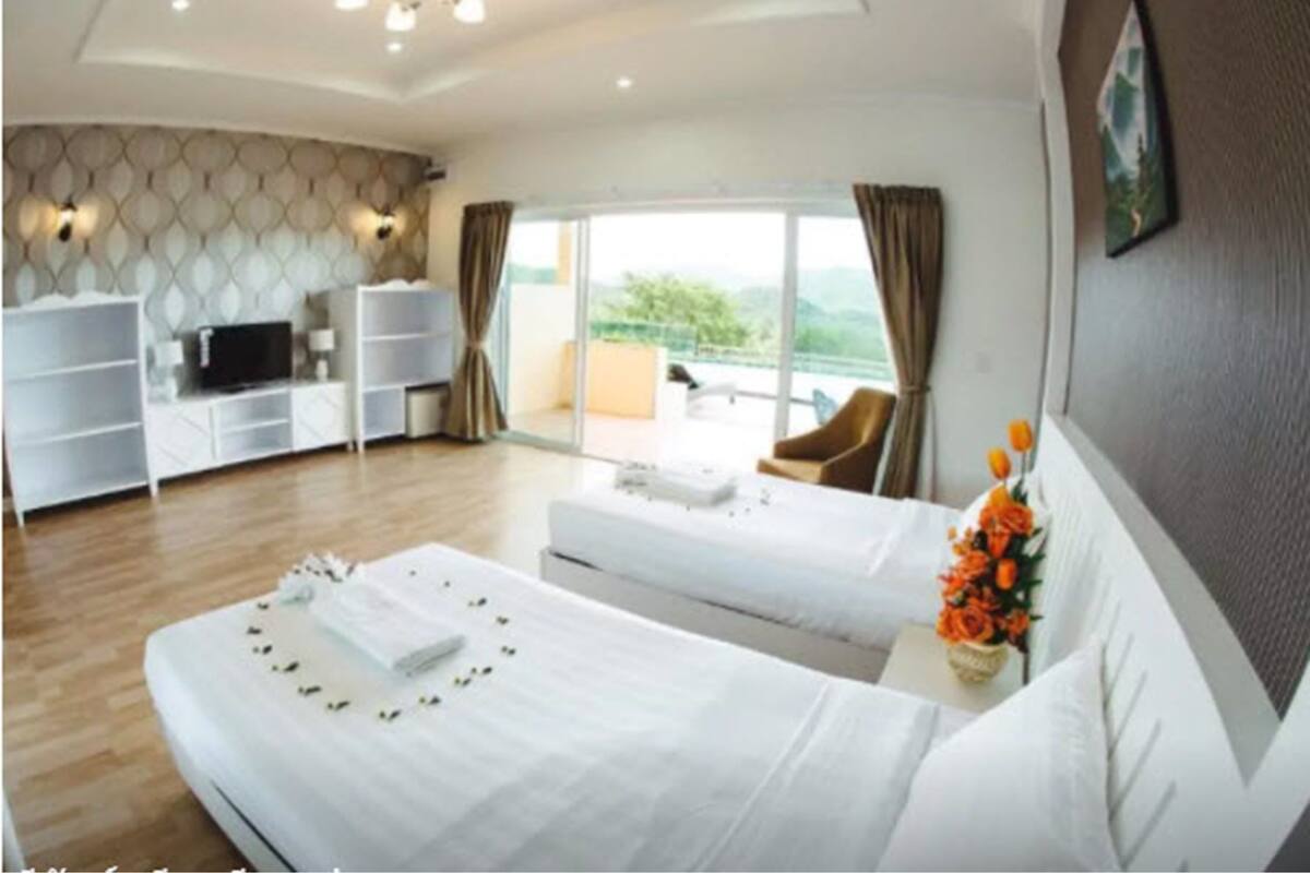 Habitación de hotel con dos camas, televisor, sofá, balcón con una silla y vistas a zonas verdes.
