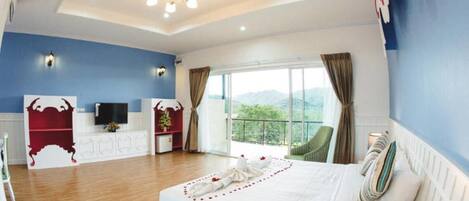 Un dormitorio amplio con una cama grande, televisión, cómoda y balcón con vistas.