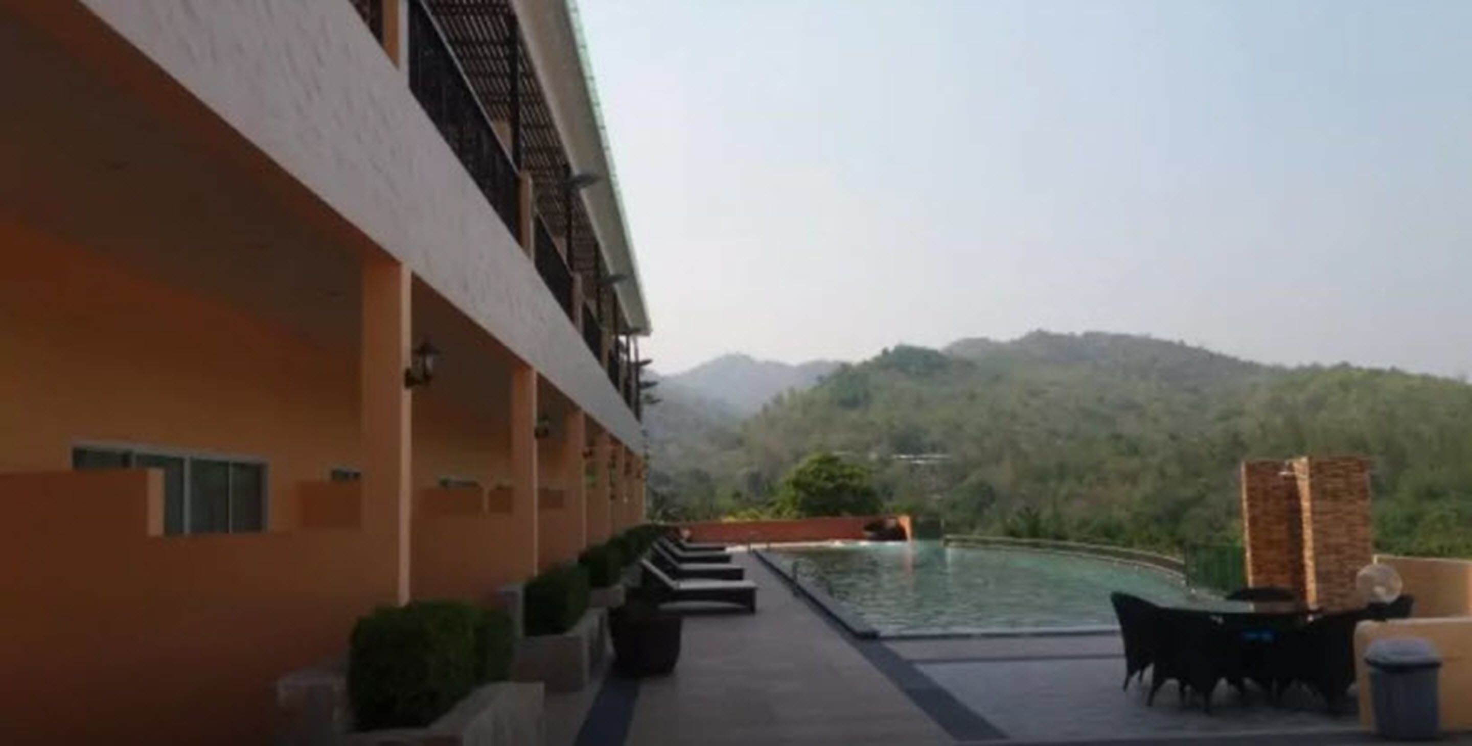 A hotel with a pool area, outdoor seating, and a view of a forested hill.