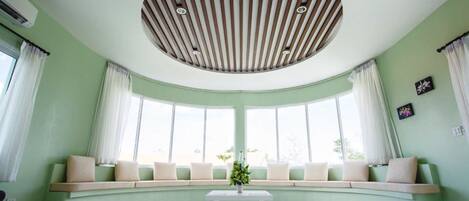 Una habitación con un asiento junto a una ventana curva, una mesa blanca en el centro y un diseño circular en el techo.