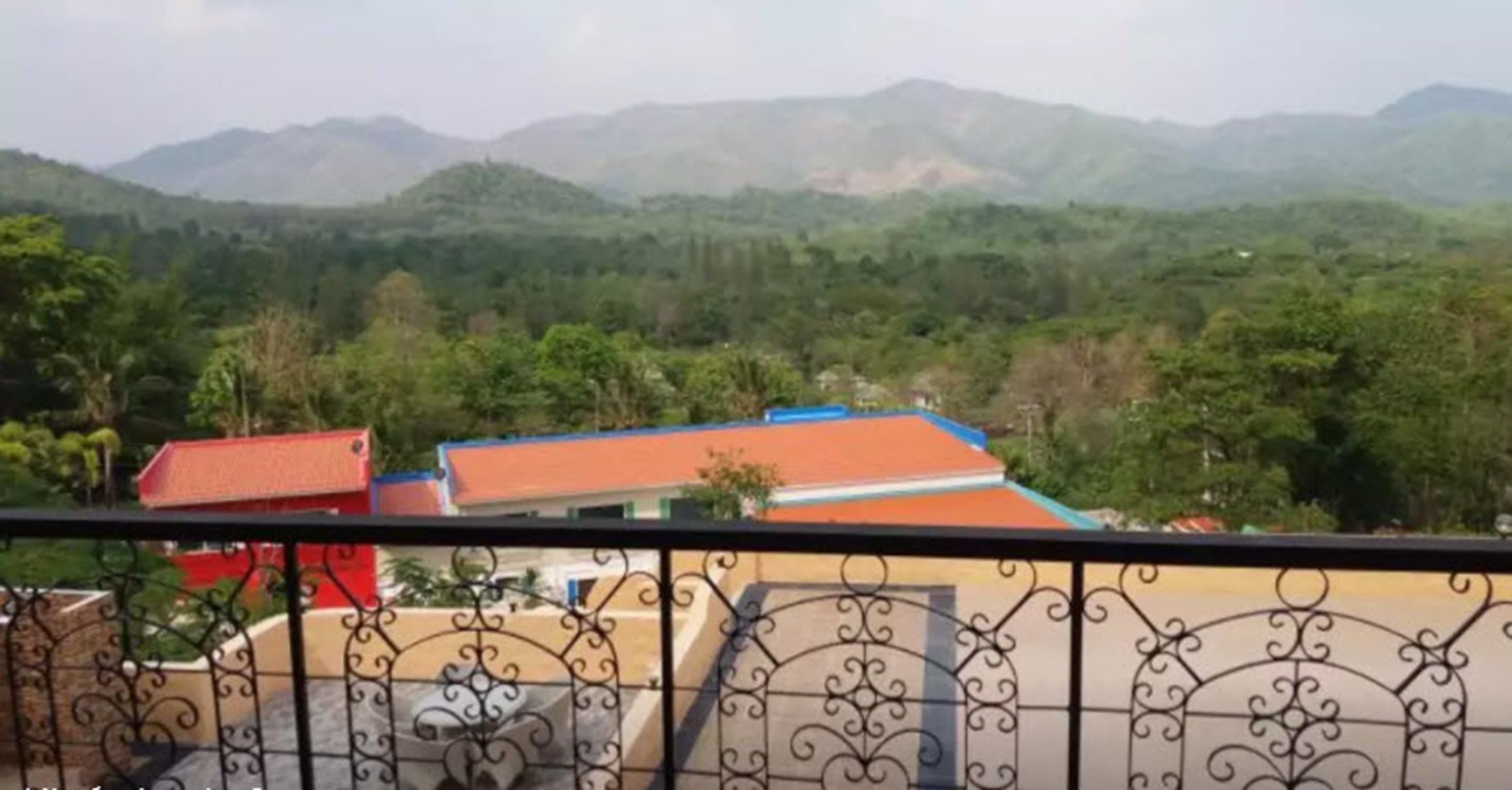 A balcony with a wrought iron railing overlooking a mountainous landscape with buildings in the foreground.