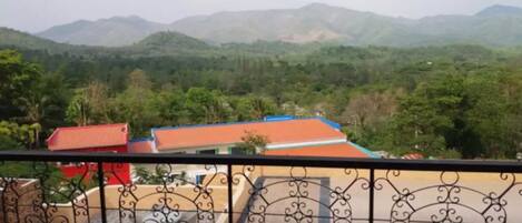 A balcony with a wrought iron railing overlooking a mountainous landscape with buildings in the foreground.