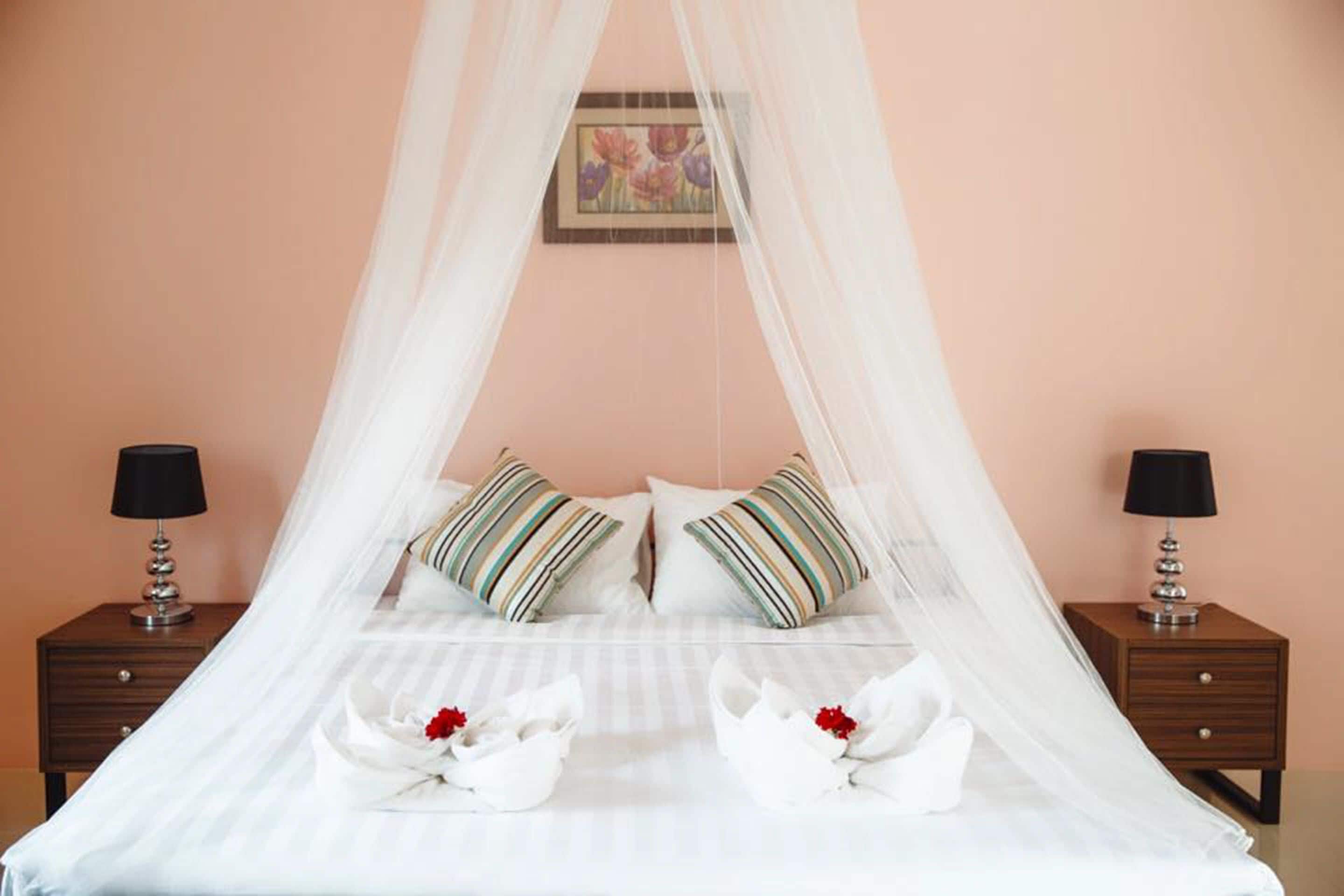 Una cama bien hecha con dosel, dos mesitas de noche con lámparas y un cuadro enmarcado en la pared.