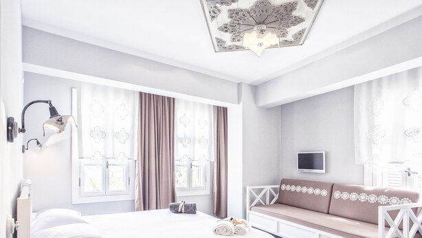 Un dormitorio moderno con una cama grande, un sofá blanco, un televisor y un ventilador de techo.