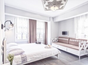 Un dormitorio moderno con una cama grande, un sofá blanco, un televisor y un ventilador de techo.