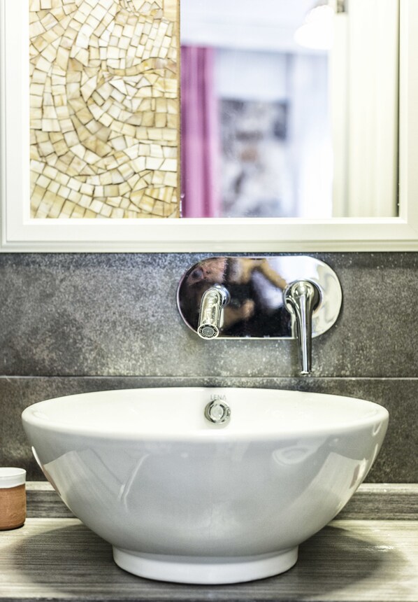 Un baño con un lavamanos blanco tipo recipiente, un espejo y una pared con mosaicos.