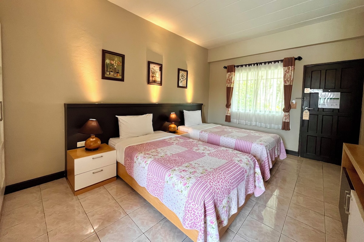 A hotel room with two beds, a nightstand, a dresser, and a door with a lock.