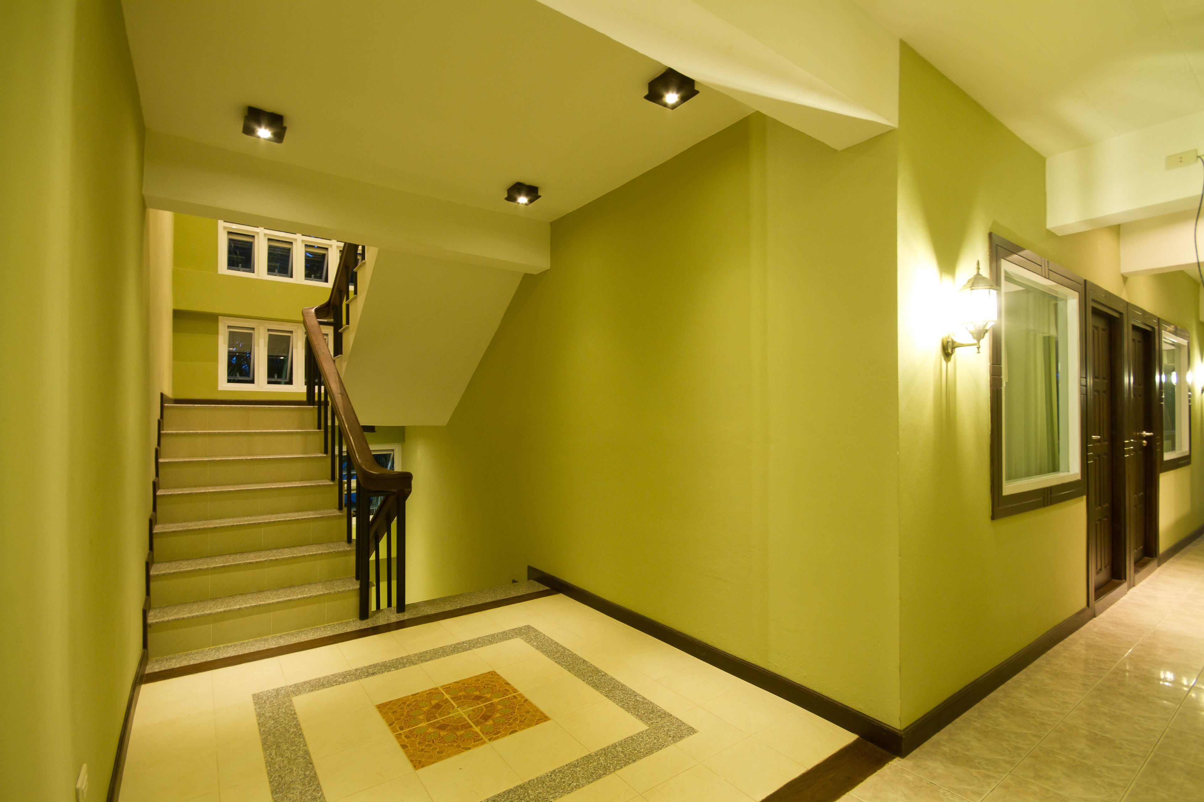 Un couloir d’hôtel avec un escalier, un sol à motifs et une porte dotée d’un miroir.