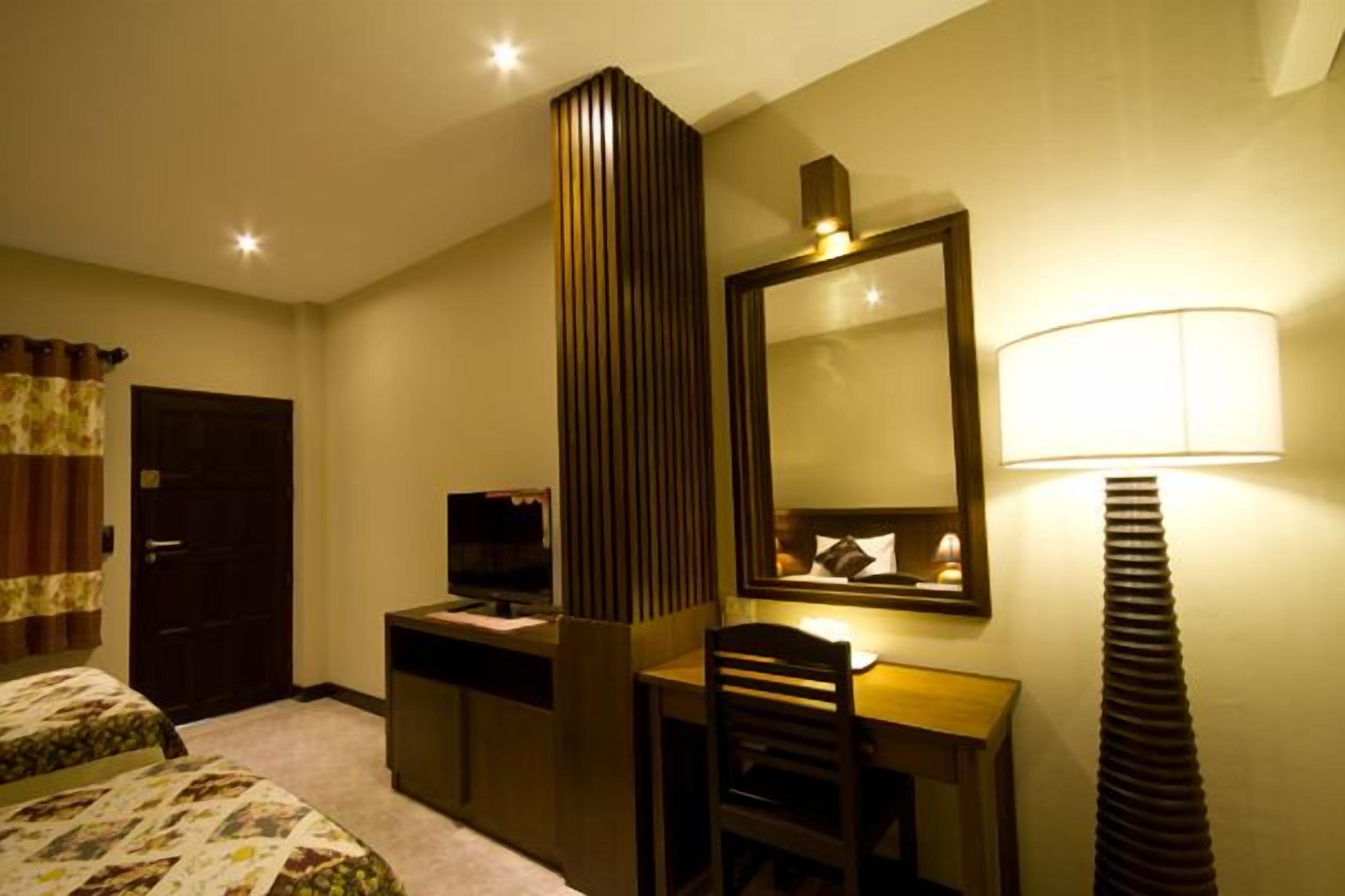 Una habitación de hotel con cama, escritorio, silla, televisor, espejo y lámpara.