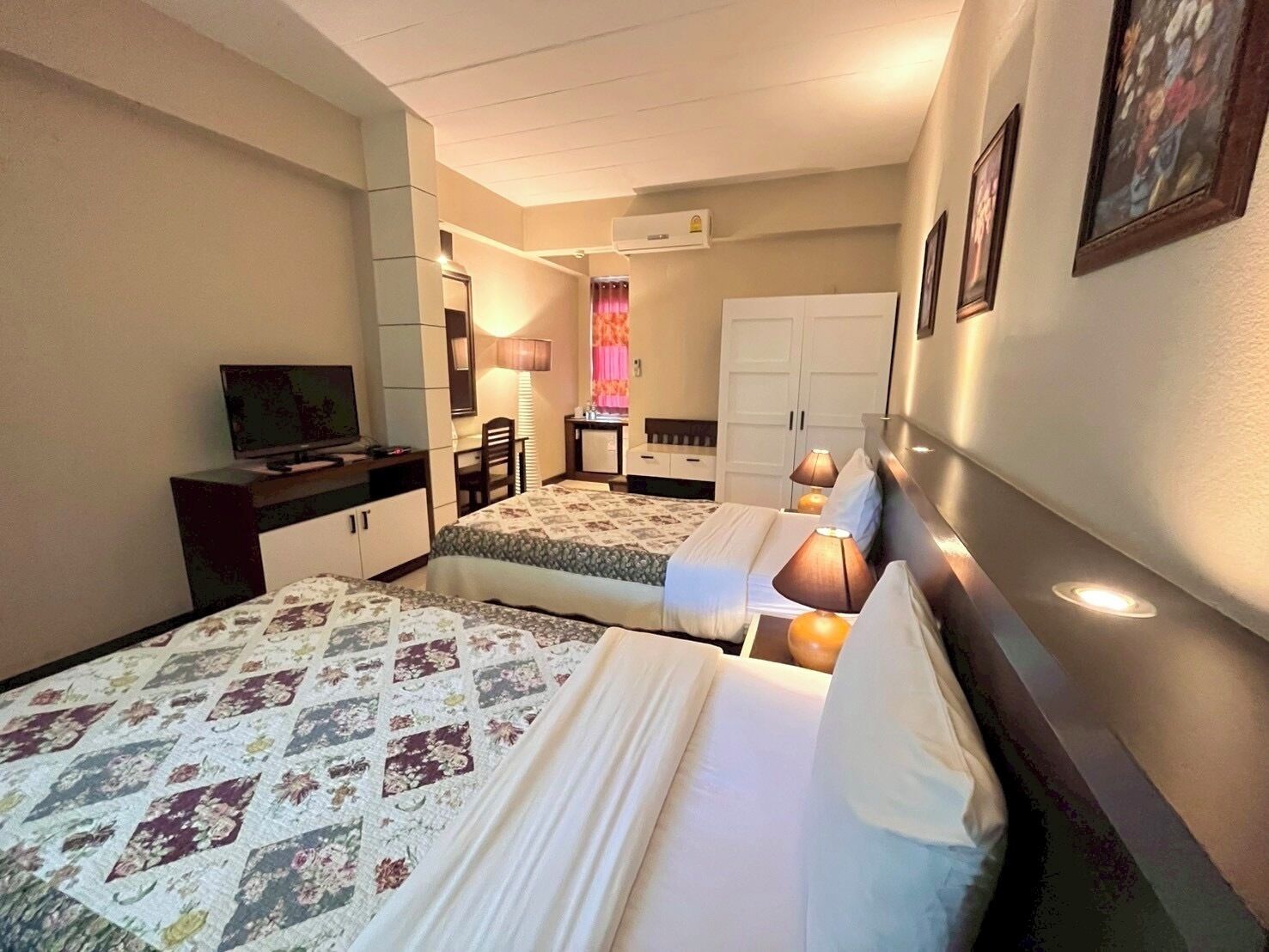 A hotel room with two beds, a desk, a TV, and a wardrobe.