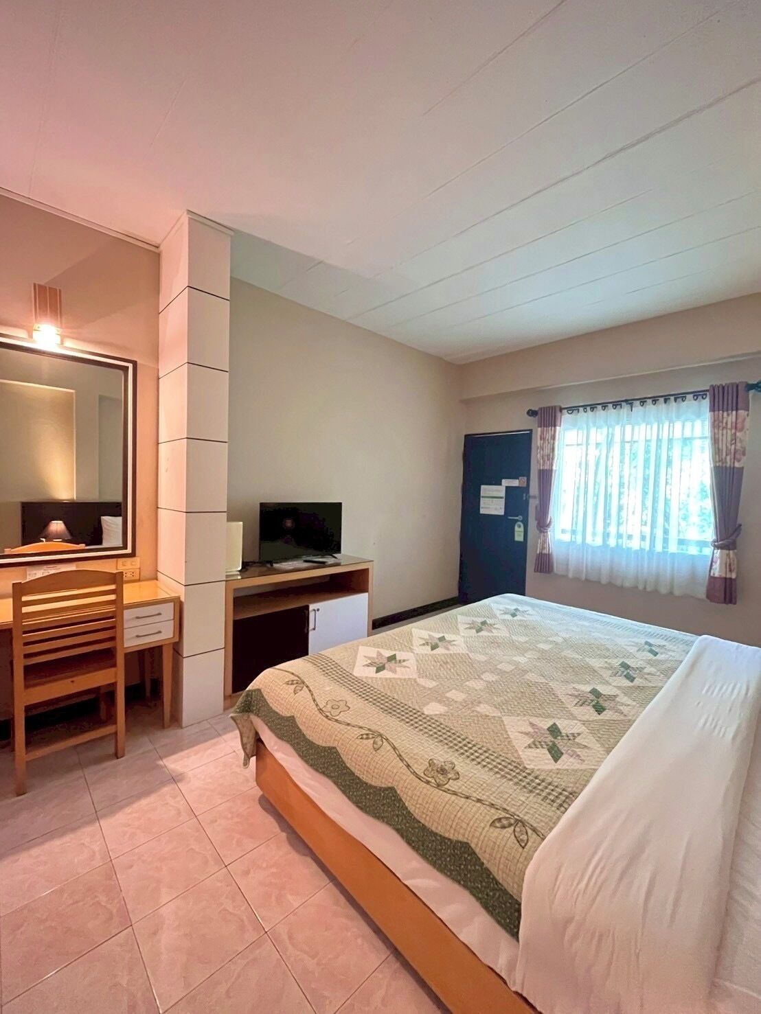 A bedroom with a bed, a desk, a chair, a mirror, and a window with curtains.