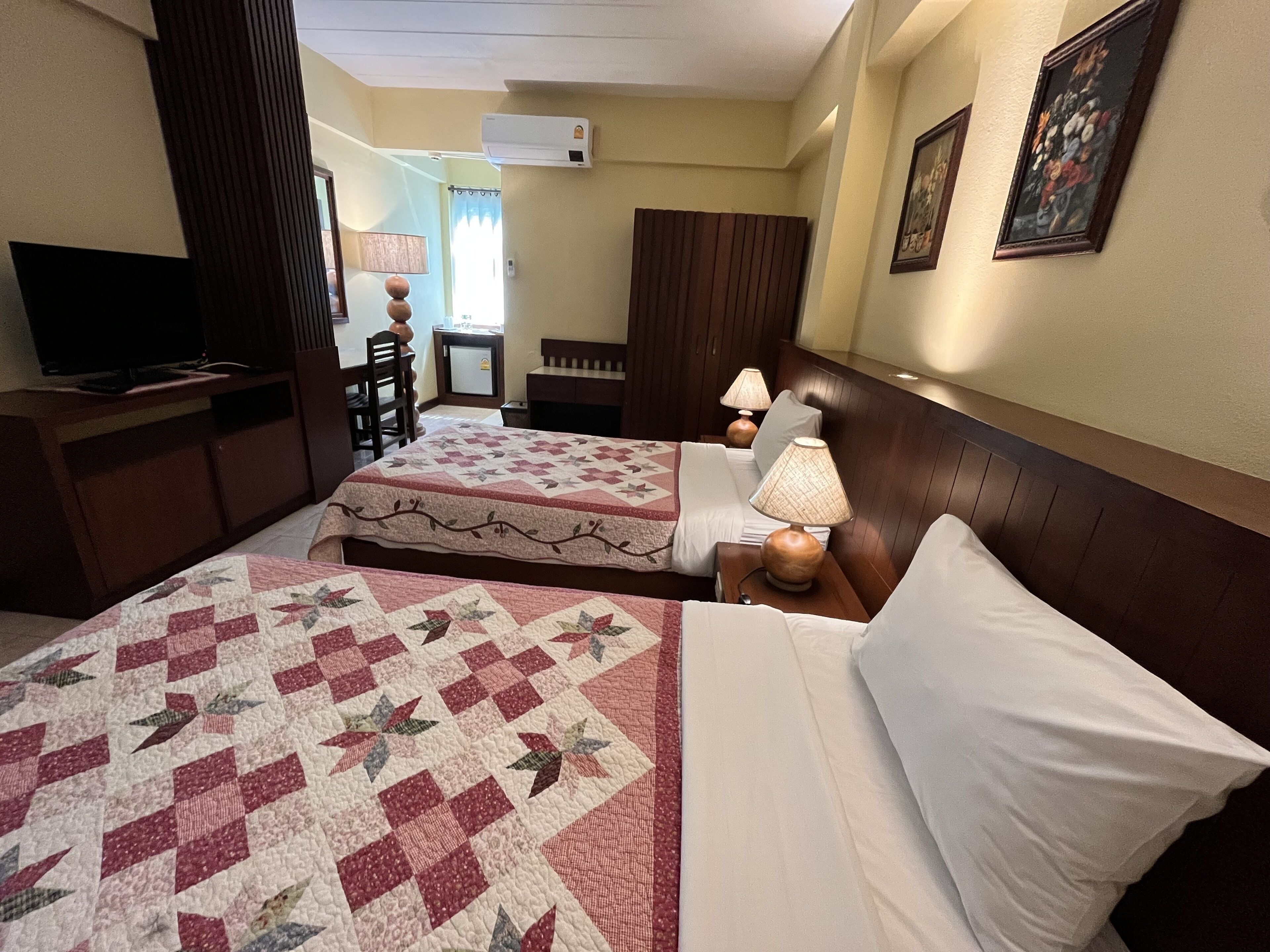 Quarto de hotel com duas camas, uma televisão, uma secretária e uma cadeira.
