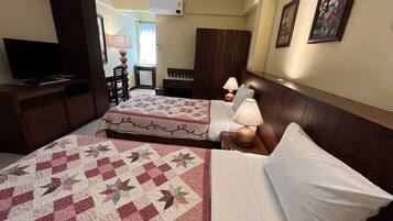 Quarto de hotel com duas camas, uma televisão, uma secretária e uma cadeira.