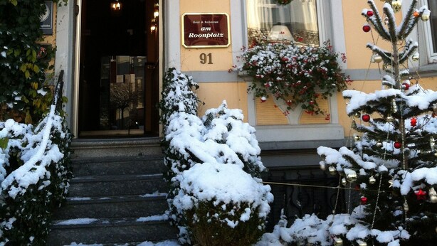 A hotel entrance with a snow-covered entrance, a sign reading "Am Roonplatz", and a Christmas tree decorated with ornaments. - Hotel Am Roonplatz (Bonn)