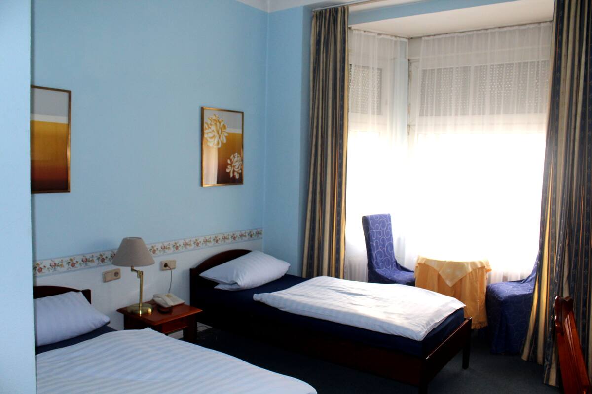 A hotel room with two beds, a chair, a lamp, and a window with curtains.