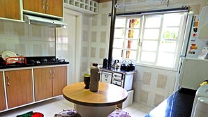 A kitchen with a round table, stools, a stove, and a refrigerator. - Residencial Encantos da Natureza (Canela)