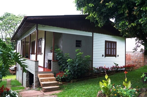 A single-story house with a porch, brick foundation, and a small garden with various plants and flowers.