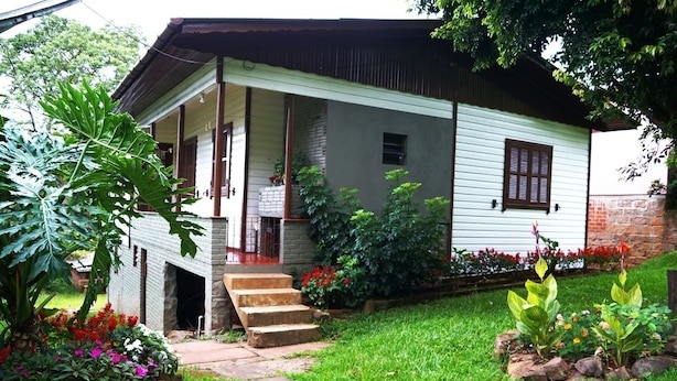 A single-story house with a porch, steps leading to the entrance, and a garden with various plants and flowers. - Residencial Recanto do Sossego Gramado (Gramado)