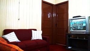 A living room with a red sofa, a television on a stand, and a wooden door in the background. - Residencial Recanto do Sossego Gramado (Gramado)