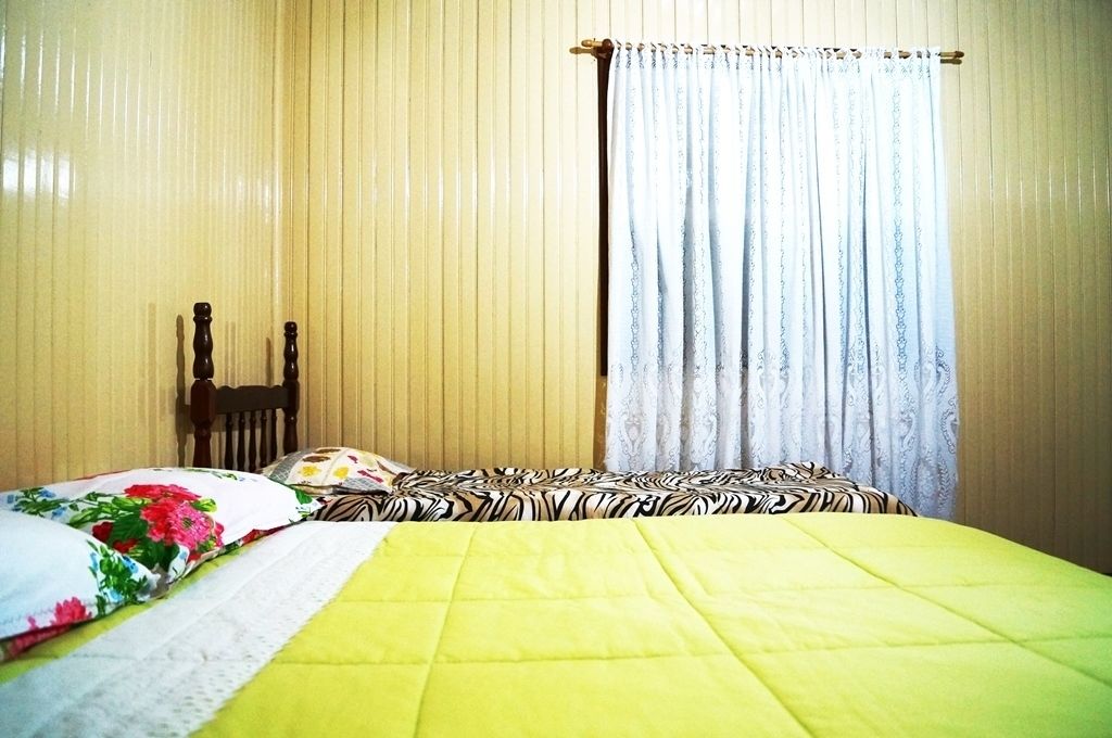 Une pièce avec un lit, une chaise en bois et une fenêtre avec des rideaux.