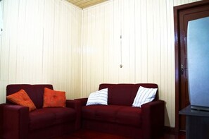 A corner room with two red sofas, one with orange and one with white and blue striped pillows.