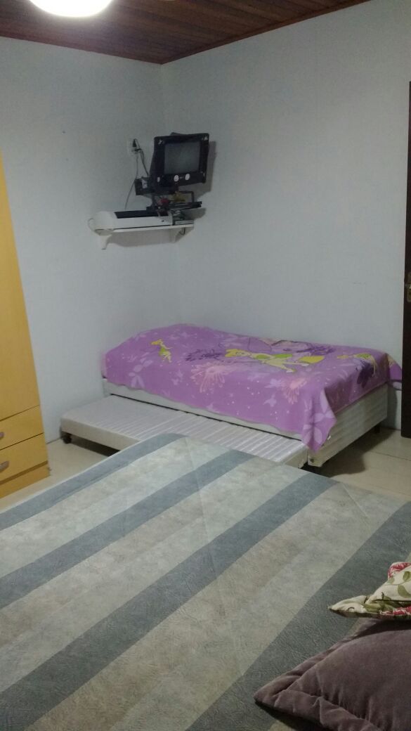 Un dormitorio con cama, una pequeña estantería con televisor y una ventana.