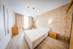 A modern bedroom with a large bed, wooden flooring, a wardrobe, a bedside table, and a hanging light fixture.