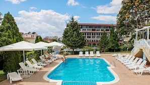 A swimming pool with lounge chairs and umbrellas, surrounded by buildings and trees. - Panorama Fort Beach Complex (Sveti Vlas)