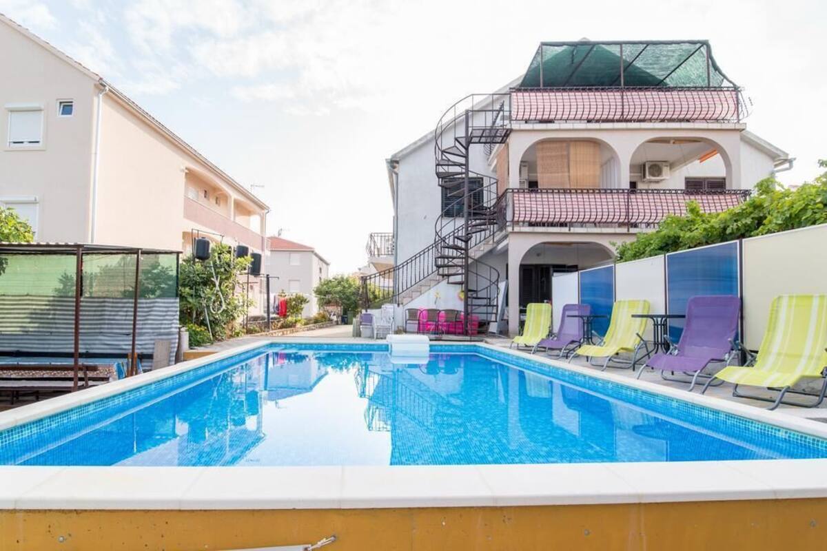 A swimming pool with lounge chairs, a staircase leading to a balcony, and a building with a modern design.