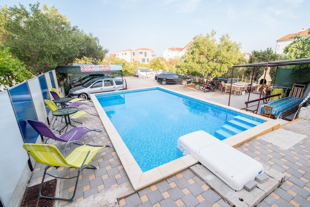 A swimming pool with a tiled deck, surrounded by colorful chairs and a covered area with a sign.