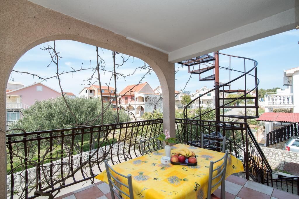 A balcony with a yellow tablecloth, a metal chair, and a fruit bowl.