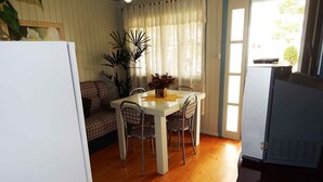 Ein kompakter Wohnraum mit Essbereich, einer Couch, einem Tisch mit Stühlen, einer Topfpflanze und einem Fernseher.